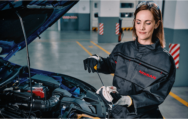 Eine Mechanikerin von Nissan überprüft den Ölstand eines Autos in einer Werkstatt, die Motorhaube ist geöffnet.